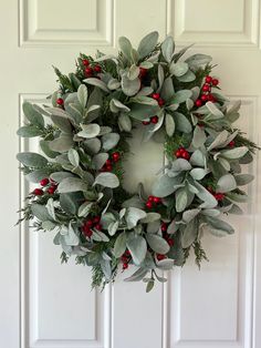 a wreath with red berries and greenery hangs on the front door's white paneled wall