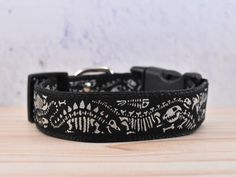 a black and white dog collar with skeleton designs on it's side, sitting on a wooden surface