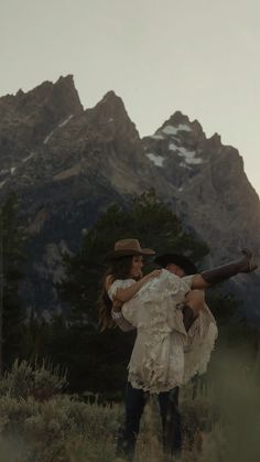 a man carrying a woman on his back while standing in the grass with mountains behind him