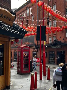 people are walking down the street in front of red telephone booths and chinese lanterns hanging above them