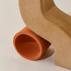 an orange vase sitting on top of a white table next to a wooden object that looks like a curved tube