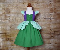 a green and purple dress on a mannequin head stand against a wooden wall