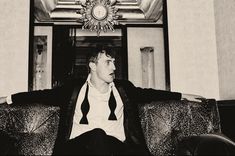 a black and white photo of a man sitting on a couch in front of a clock