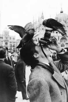 a man holding a camera up to his face with two birds perched on his head