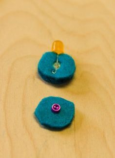 two small blue buttons sitting on top of a wooden table next to a yellow button