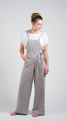 a woman standing in front of a white background wearing grey overalls and a white t - shirt