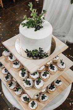 a three tiered cake and cupcakes on wooden trays with greenery