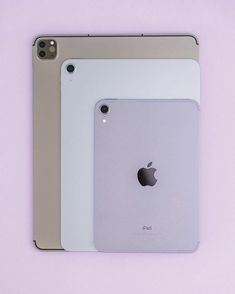 two ipads sitting next to each other on a purple surface with the same apple logo