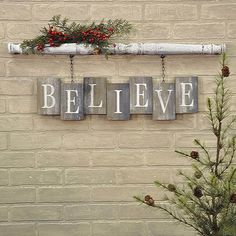 a sign that says believe hanging on the side of a brick wall next to a small christmas tree