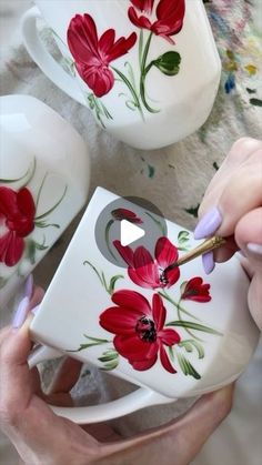 a woman is painting red flowers on a coffee cup