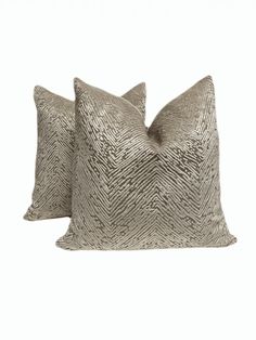 two silver pillows sitting next to each other on top of a white surface with one pillow in the shape of a zigzag pattern