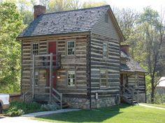 an old log cabin with a red door and stairs on the front porch, next to a white pickup truck