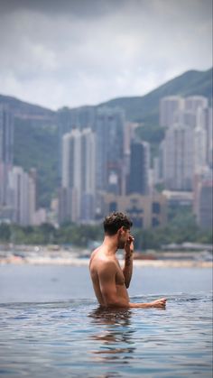 a man is sitting in the water and talking on his cell phone while looking at the city