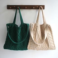 two knitted bags hanging on a wooden coat rack in front of a white wall