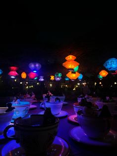 many lit up tea cups and saucers are on the table in front of some lights