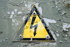 a yellow and black hazard sign on a gray wall with peeling paint chipping off it