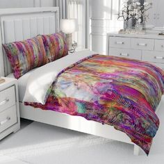 a bed with a colorful comforter on top of it next to a night stand