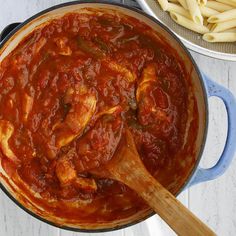 a pot filled with pasta and sauce next to a wooden spoon on top of a table