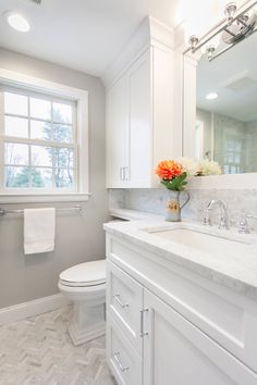 a bathroom with white cabinets and marble counter tops, along with a large mirror over the toilet