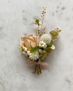 a boutonniere with flowers and greenery on a marble surface