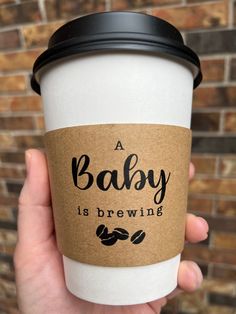 a person holding up a coffee cup with the words baby is brewing on it's side