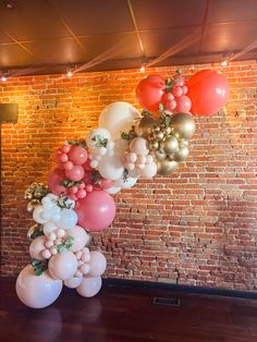 a bunch of balloons that are hanging from the ceiling in front of a brick wall