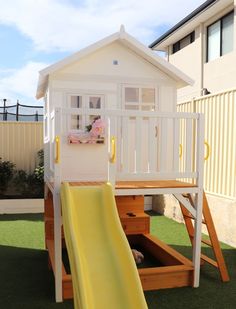 a small white house with a yellow slide in the grass next to it's deck