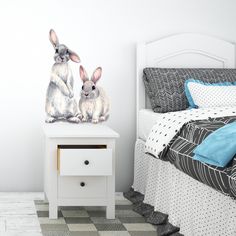 two rabbits sitting on top of a white nightstand next to a bed