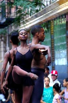 two dancers in black leotards are dancing on the street while people watch from the sidewalk