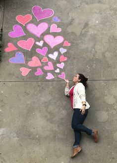 a woman drawing hearts on the sidewalk with chalk and crayon markers in front of her