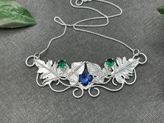 I've handmade this beautiful Woodland Leaves Elvish-inspired necklace keepsake, perfect for a Woodland wedding theme, or any event you desire! I've designed this in sterling silver with 3 gemstones. The top two are 4mm round faceted (emeralds shown in the images) and a center 6mm faceted gemstone of your choice. The pictures show 4 with a Rainbow Topaz for a lovely matching combination. Please contact me if you want specific gemstone choices not shown. I can accommodate most! Upon your order, pl Artisan Wedding Necklaces With Unique Variations, Custom Silver Necklaces For Anniversary, Artisan Birthstone Necklace For Gifts, Handmade Silver Whimsical Jewelry, Whimsical Handmade Silver Jewelry, Artisan Necklace With Decorative Details As Gift, Whimsical Handmade Necklaces For Weddings, Artisan Decorative Necklaces For Gifts, Artisan Decorative Necklace For Gifts