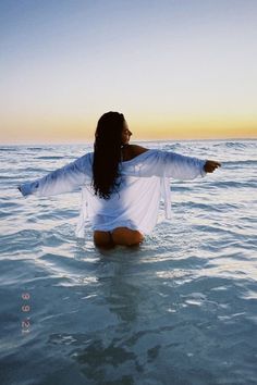 a woman is sitting in the water with her arms spread out and looking at the sky