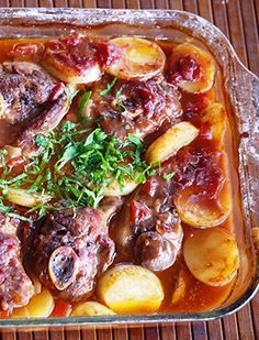 a casserole filled with meat and potatoes on top of a wooden table next to a fork