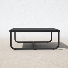 a black coffee table sitting on top of a cement floor next to a white wall