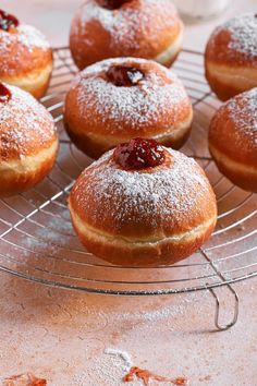 powdered sugar covered doughnuts on a wire rack with cherries in the middle