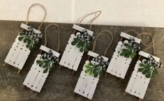 four white wooden pegs with green leaves and bows on them are hanging from twine