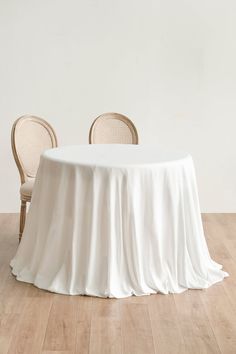 two chairs and a table with a white cloth on it in front of a wall