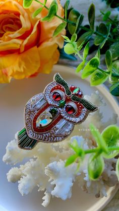 an owl brooch sitting on top of a white plate next to a yellow rose