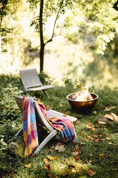 two chairs and a fire pit in the middle of a field with leaves on the ground