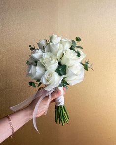 a bouquet of white roses is held by a woman's hand in front of a gold wall