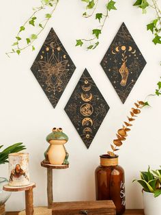 three wall hangings with plants and vases on top of the table in front of them