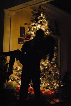 a man standing in front of a christmas tree with his arms wrapped around the neck