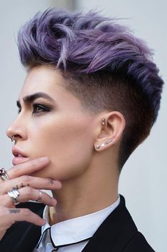 a woman with purple hair and piercings on her ear looking off to the side