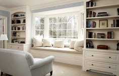 a white chair sitting in front of a window next to a book shelf filled with books