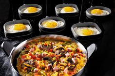 a pan filled with eggs and sausages on top of a black counter next to other cooking utensils