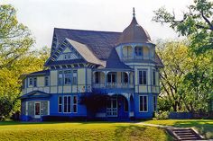 a large blue and white house sitting on top of a lush green field next to trees