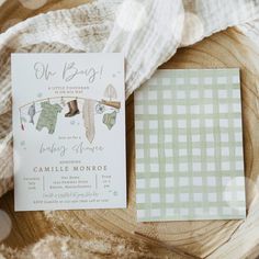 a baby shower is displayed on a wooden plate next to a card with clothes hanging from a line