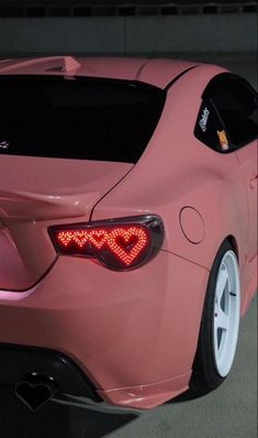 a pink sports car parked in a parking lot at night with its tail lights on