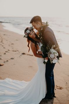 a bride and groom standing on the beach with their arms around each other as they kiss