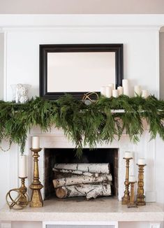 a mantel with candles and greenery on it in front of a mirror above the fireplace